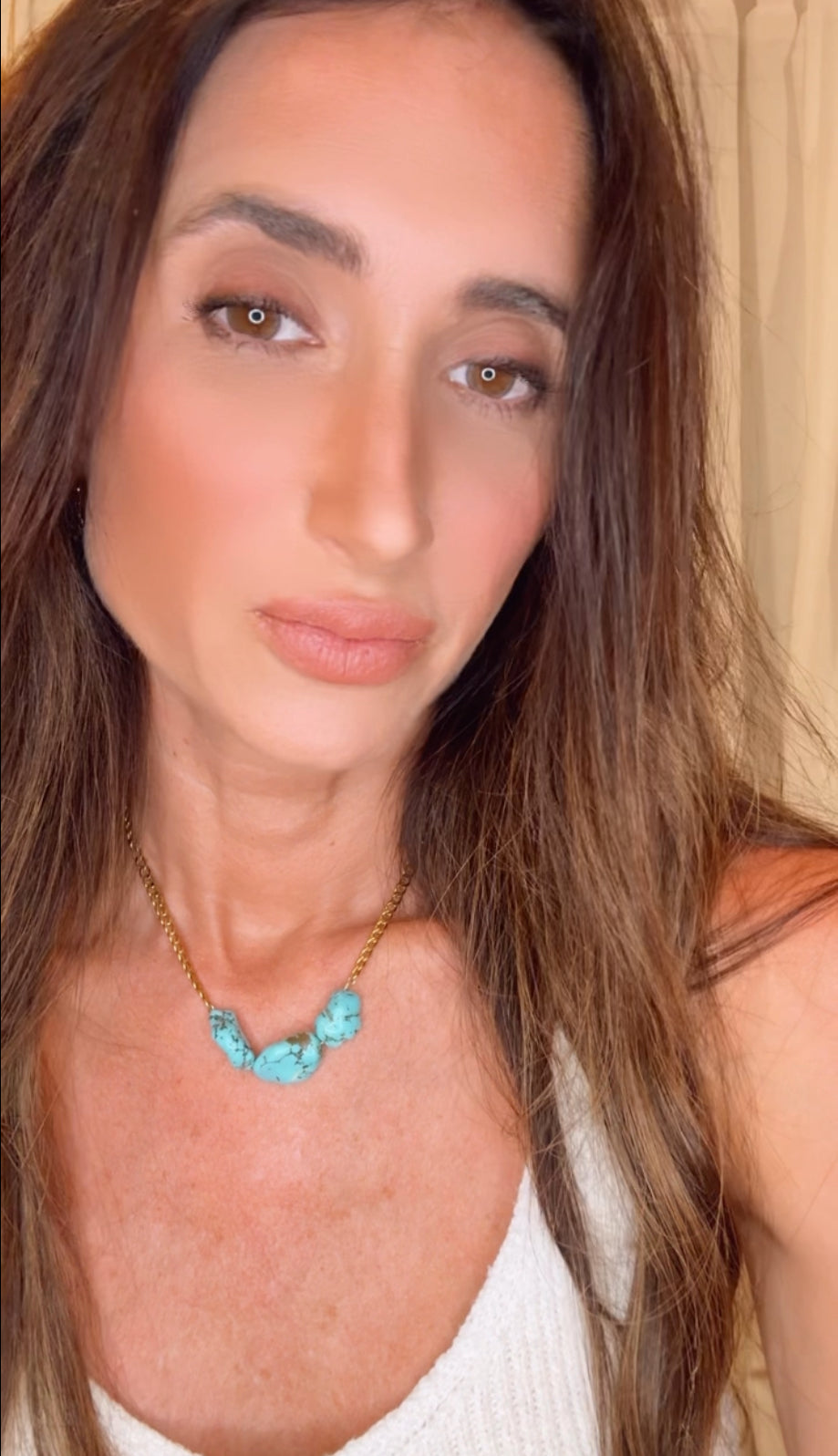 Woman wearing a necklace with turquoise beads against a neutral background