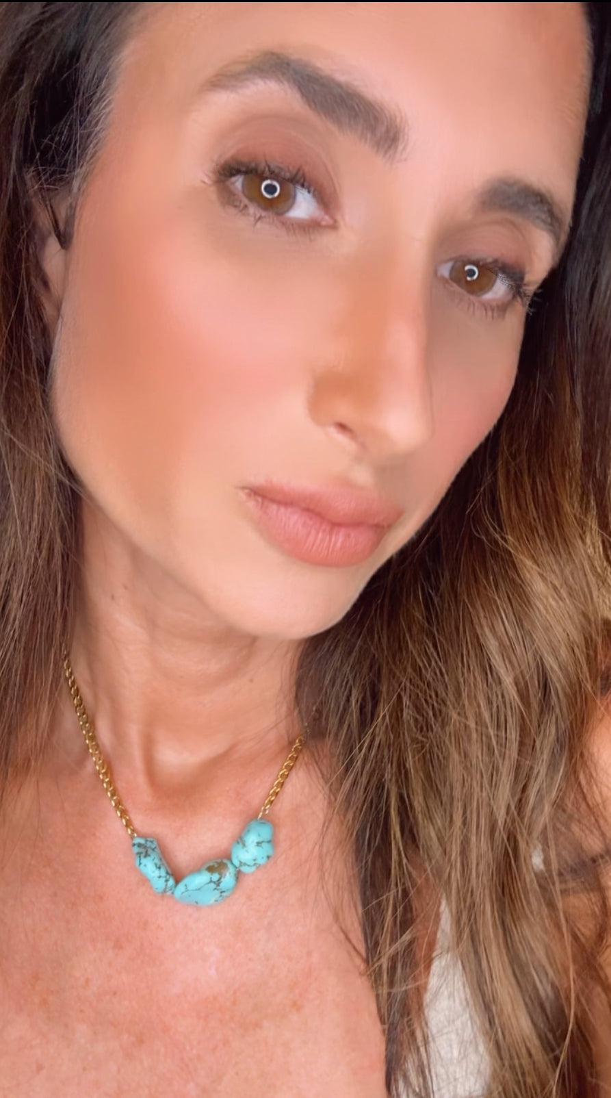 Close-up of a person wearing a turquoise necklace with gold chain